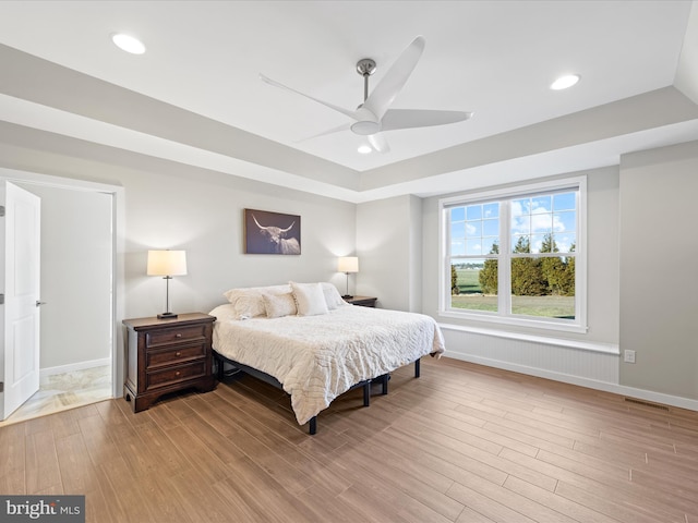 bedroom with a tray ceiling, wood finished floors, visible vents, and recessed lighting