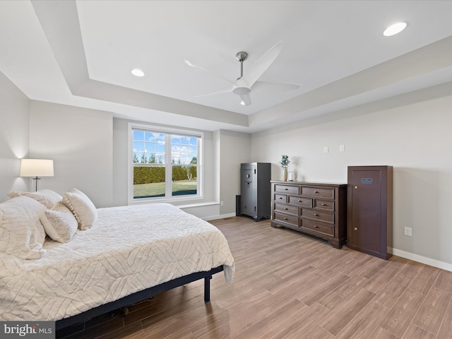 bedroom featuring light wood finished floors, baseboards, a raised ceiling, and recessed lighting