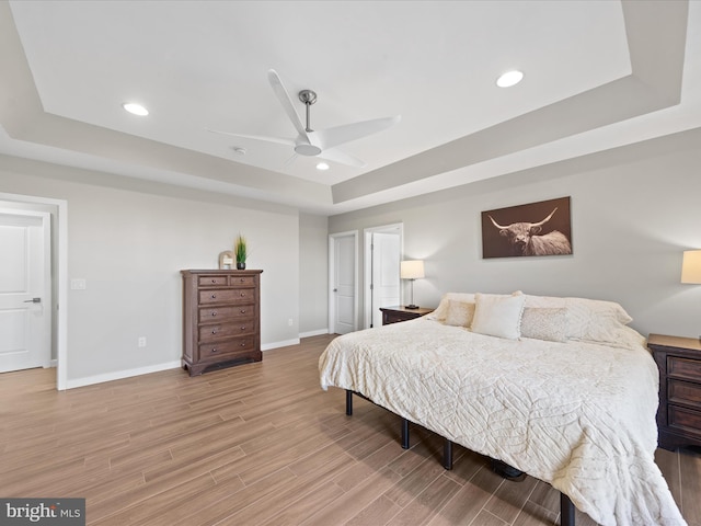 bedroom featuring light wood-type flooring, baseboards, a tray ceiling, and recessed lighting