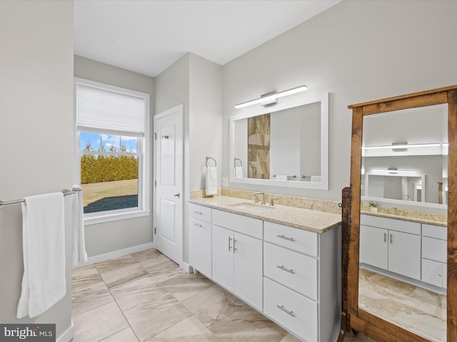 full bath with marble finish floor, two vanities, a sink, and baseboards