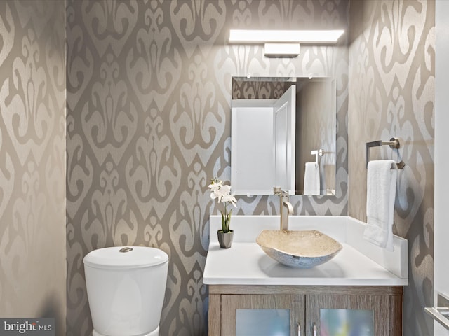 bathroom featuring toilet, wallpapered walls, and vanity