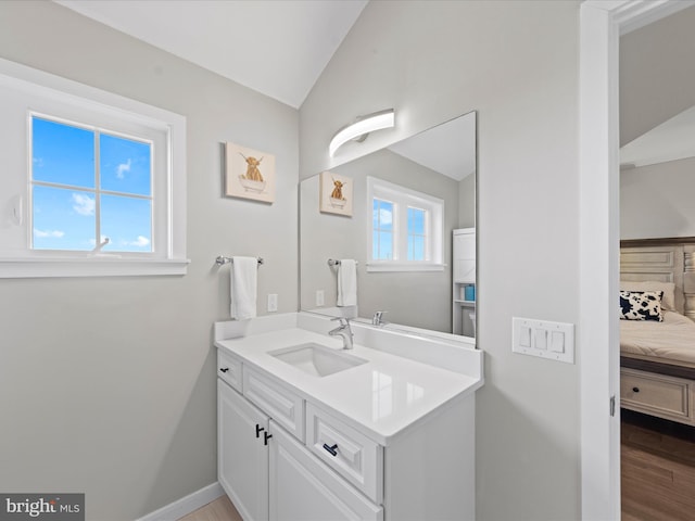 ensuite bathroom featuring baseboards, connected bathroom, lofted ceiling, wood finished floors, and vanity