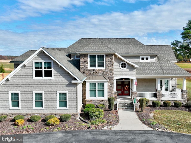 view of front of property with stone siding, covered porch, french doors, and roof with shingles