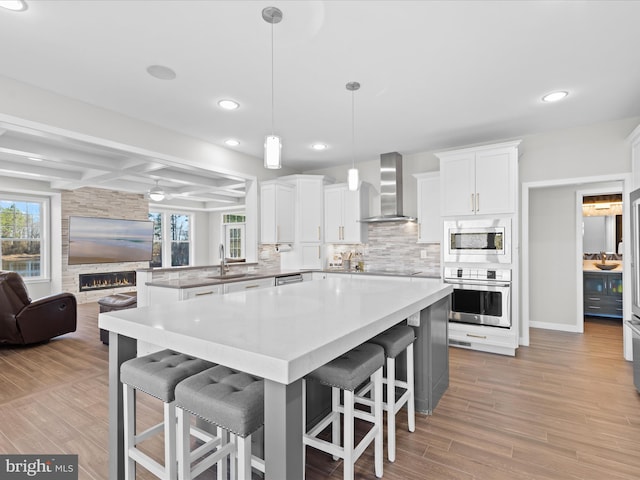 kitchen featuring coffered ceiling, wall chimney exhaust hood, appliances with stainless steel finishes, a sink, and backsplash