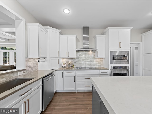 kitchen featuring wall chimney range hood, dark wood-type flooring, appliances with stainless steel finishes, and white cabinets