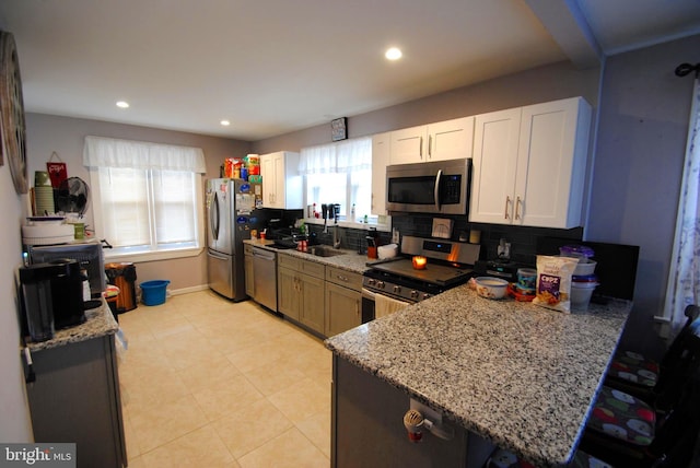 kitchen featuring sink, kitchen peninsula, appliances with stainless steel finishes, light stone counters, and white cabinetry