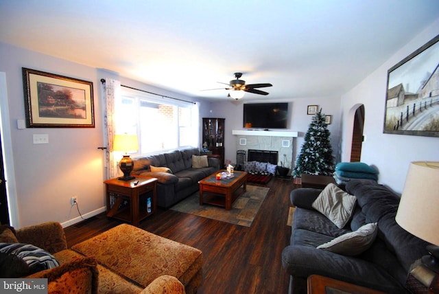 living room with a stone fireplace, ceiling fan, and dark hardwood / wood-style floors