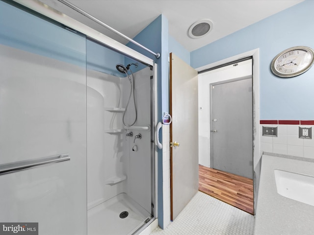 bathroom with tile walls, a shower with door, sink, and tile patterned floors