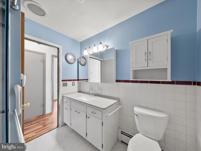 bathroom with tile patterned flooring, toilet, vanity, tile walls, and a baseboard radiator