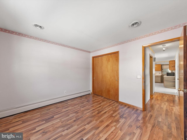 unfurnished bedroom with a closet, wood-type flooring, and a baseboard heating unit