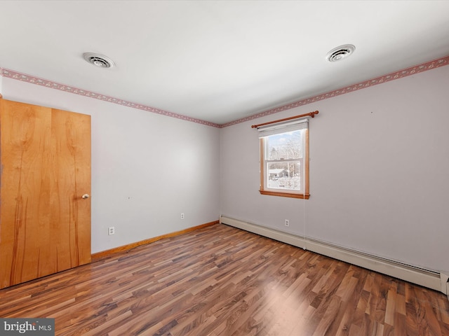 unfurnished room featuring baseboard heating and hardwood / wood-style floors