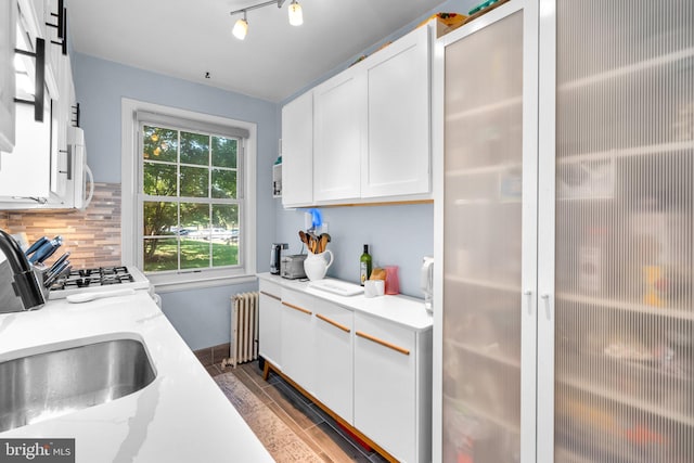 kitchen with radiator, sink, range, white cabinetry, and backsplash