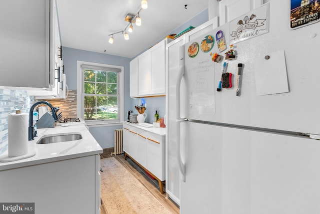 kitchen featuring sink, white refrigerator, radiator heating unit, white cabinets, and backsplash