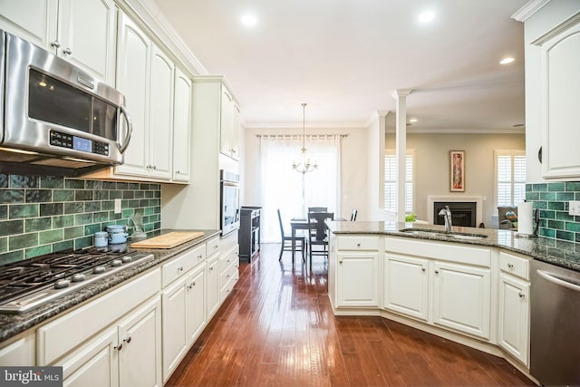 kitchen featuring dark stone countertops, stainless steel appliances, sink, white cabinetry, and decorative light fixtures