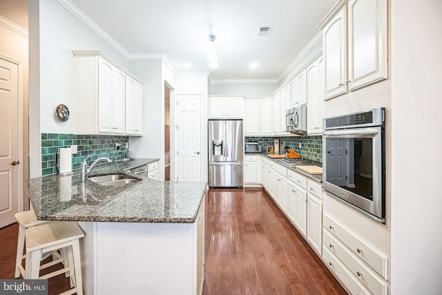 kitchen featuring stainless steel appliances, kitchen peninsula, dark stone counters, white cabinets, and sink