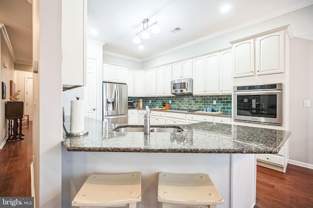 kitchen with stainless steel appliances, dark stone counters, white cabinets, and a kitchen breakfast bar