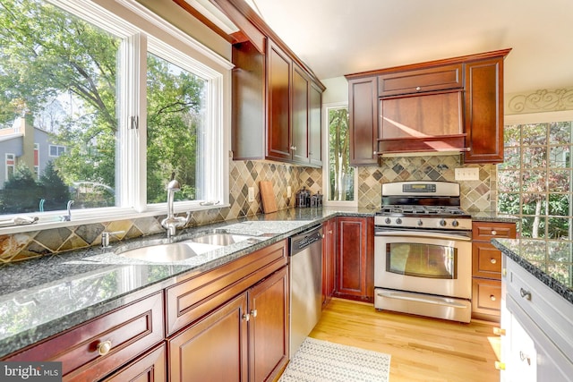 kitchen featuring sink, dark stone countertops, stainless steel appliances, light hardwood / wood-style floors, and backsplash