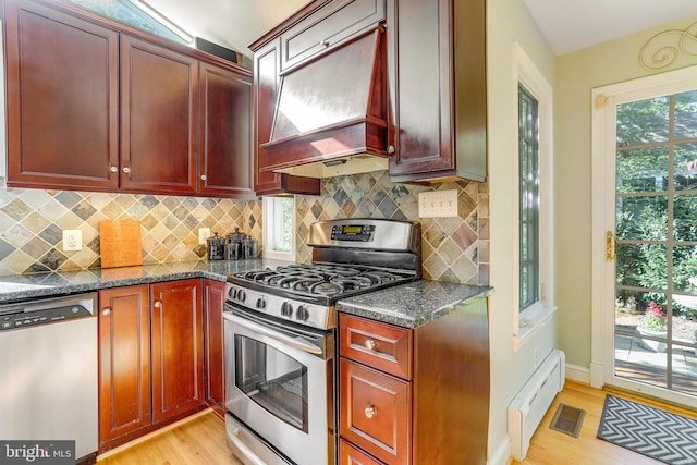 kitchen featuring a baseboard radiator, stainless steel appliances, custom exhaust hood, and dark stone counters