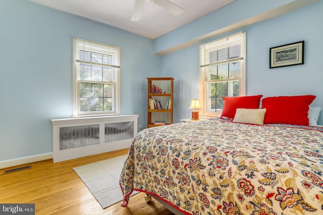 bedroom with ceiling fan, radiator heating unit, multiple windows, and light hardwood / wood-style flooring