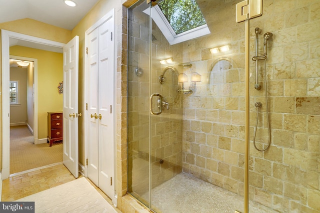 bathroom with vaulted ceiling with skylight and a shower with shower door