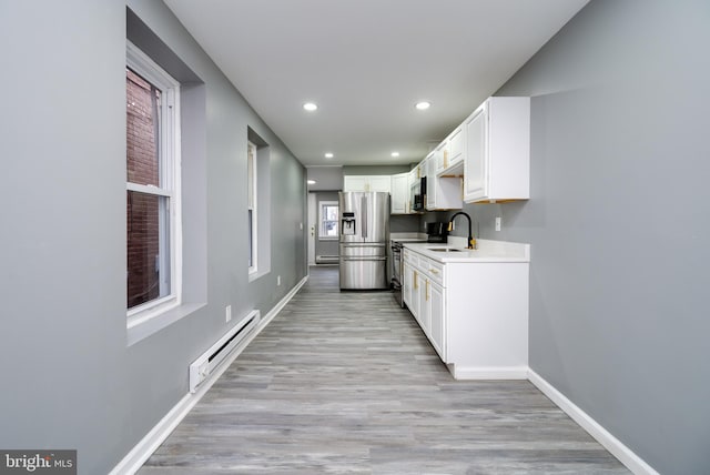 kitchen with white cabinets, stainless steel appliances, a baseboard radiator, and light wood-type flooring