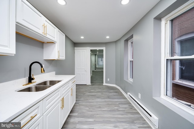 kitchen with a baseboard heating unit, white cabinets, sink, light wood-type flooring, and plenty of natural light