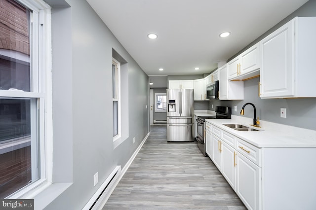 kitchen with white cabinets, sink, baseboard heating, appliances with stainless steel finishes, and light hardwood / wood-style floors