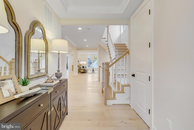 corridor with ornamental molding, light hardwood / wood-style floors, and a tray ceiling