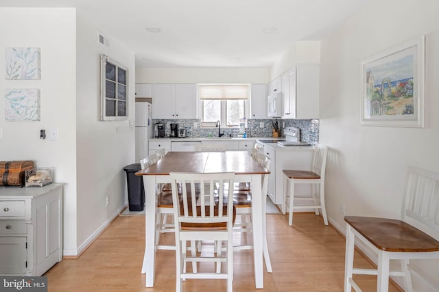 kitchen featuring backsplash, a kitchen island, a breakfast bar, white appliances, and white cabinetry