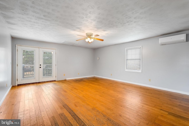 empty room with french doors, light hardwood / wood-style flooring, ceiling fan, a textured ceiling, and a wall mounted AC