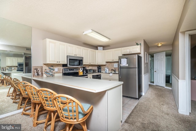 kitchen with a breakfast bar, light tile patterned floors, kitchen peninsula, and appliances with stainless steel finishes