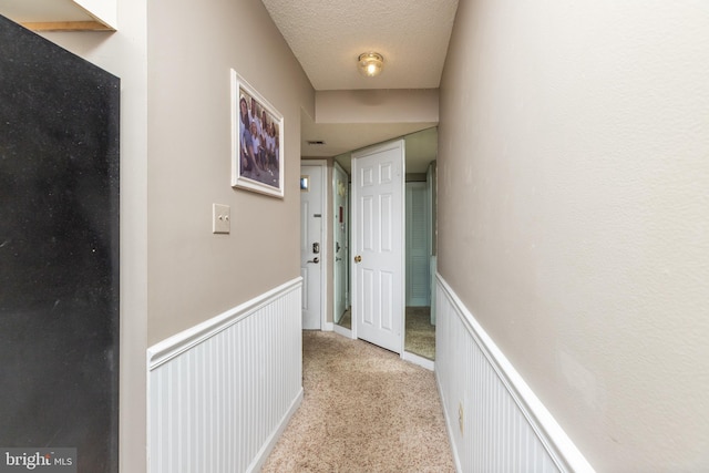 corridor with a textured ceiling and light colored carpet