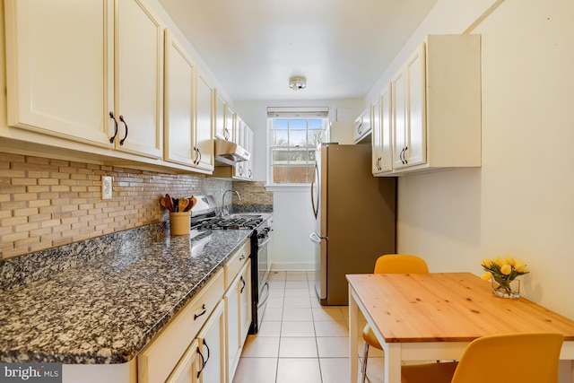 kitchen featuring tasteful backsplash, dark stone countertops, stainless steel refrigerator, light tile patterned floors, and range with gas stovetop