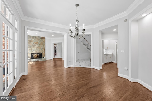 unfurnished dining area with dark wood-type flooring, a stone fireplace, ornamental molding, and a notable chandelier