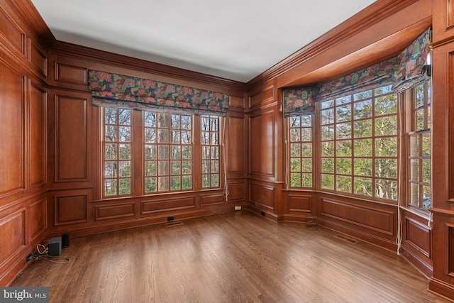 empty room with crown molding, wooden walls, and hardwood / wood-style flooring