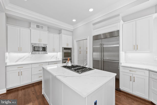 kitchen featuring light stone counters, built in appliances, white cabinetry, and a kitchen island