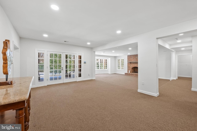 unfurnished living room with light colored carpet, a fireplace, and french doors