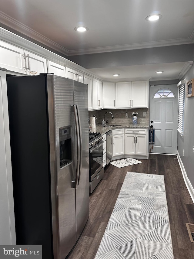 kitchen with white cabinets, ornamental molding, appliances with stainless steel finishes, and tasteful backsplash