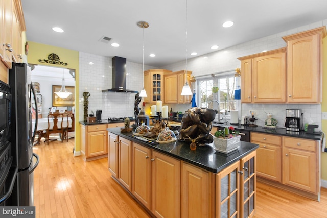 kitchen with wall chimney range hood, pendant lighting, light hardwood / wood-style floors, a kitchen island, and appliances with stainless steel finishes