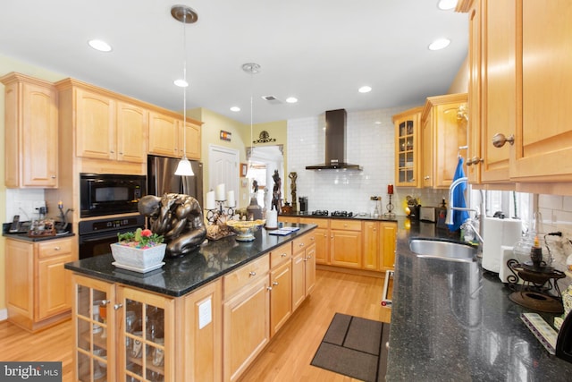 kitchen with dark stone countertops, wall chimney exhaust hood, black appliances, and decorative light fixtures