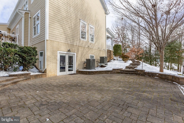 snow covered property featuring french doors, cooling unit, and a patio area