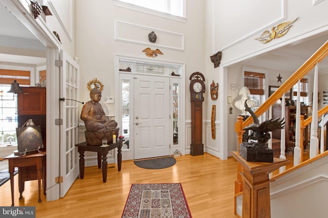 foyer entrance with a healthy amount of sunlight, a towering ceiling, crown molding, and light hardwood / wood-style flooring