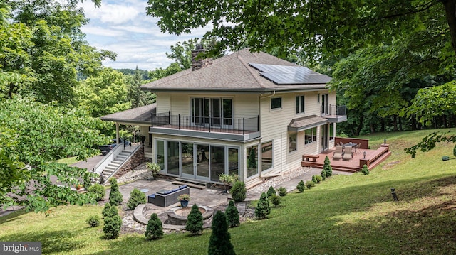 back of property with a lawn, outdoor lounge area, solar panels, a wooden deck, and a balcony