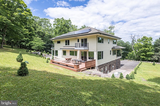 rear view of house with a lawn, solar panels, a balcony, and a wooden deck