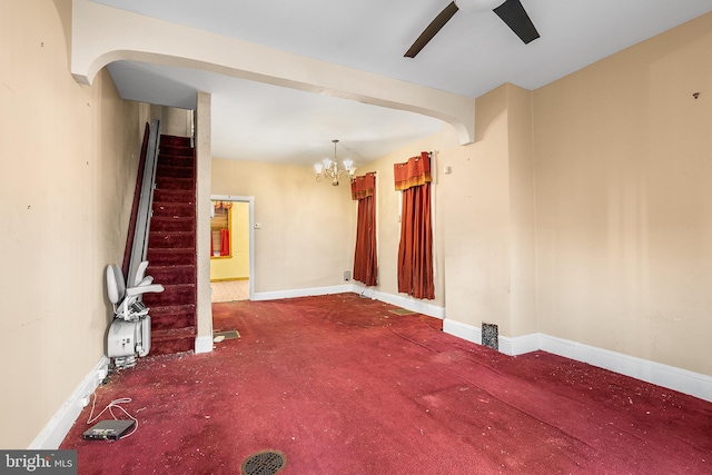 carpeted spare room featuring ceiling fan with notable chandelier