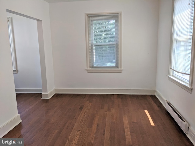 unfurnished room with dark hardwood / wood-style floors, baseboard heating, and a wealth of natural light