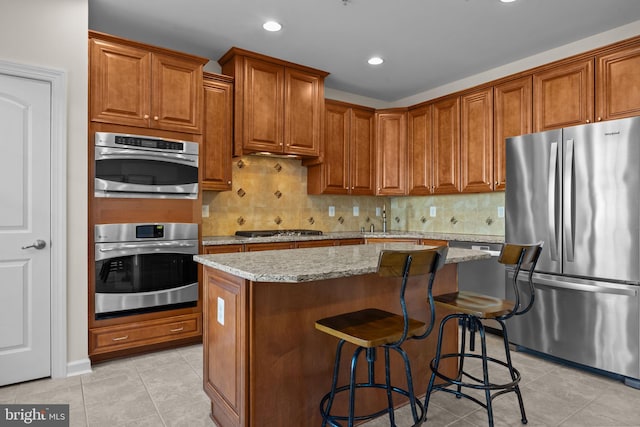 kitchen with light stone counters, appliances with stainless steel finishes, a center island, and a breakfast bar area