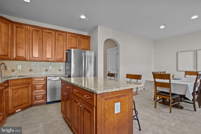 kitchen with a kitchen island, appliances with stainless steel finishes, sink, decorative backsplash, and light stone counters