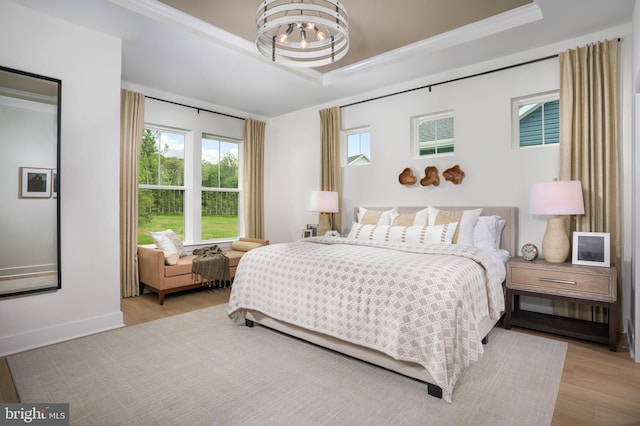 bedroom featuring a tray ceiling, light hardwood / wood-style flooring, a notable chandelier, and crown molding