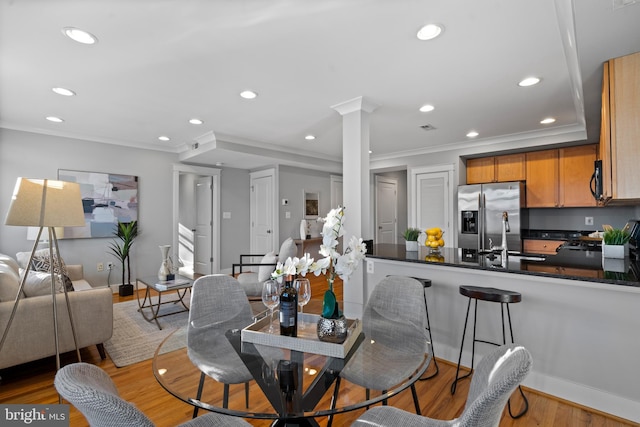 dining room featuring sink, decorative columns, light hardwood / wood-style floors, and crown molding